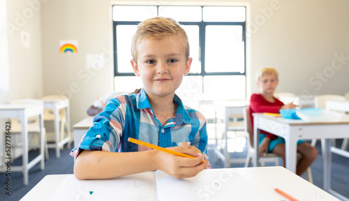 Portrait of smiling caucasian elementary schoolboy sitting at desk in school