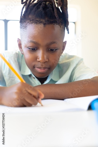 African american elementary schoolboy writing on book at desk in classroom