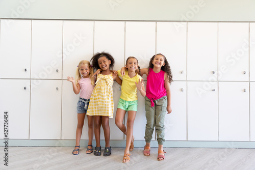 Portrait of cheerful multiracial elementary schoolgirls with arm around waiting while standing