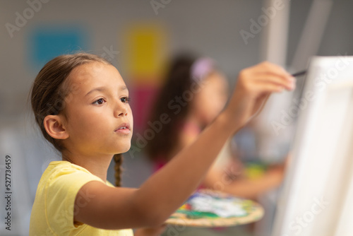 Close-up of caucasian elementary schoolgirl painting on easel in drawing class