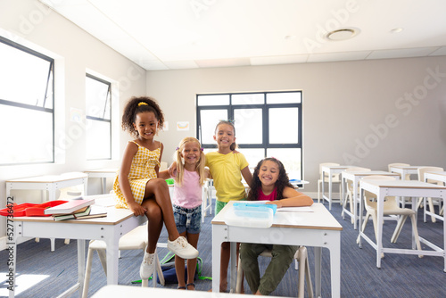 Portrait of cheerful multiracial elementary schoolgirls at desk in classroom