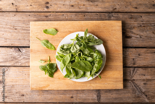 Directly above shot of fresh green baby spinach in plate on cutting board over wooden table