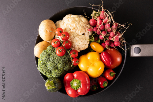 Overhead close-up of various colorful vegetables in frying pan on black background
