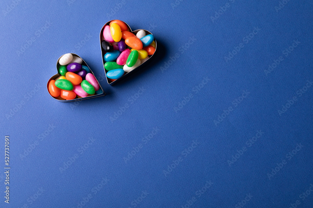 Directly above view of heart shape containers with colorful candies by copy space on blue background Directly above view of heart shape containers with colorful candies by copy space on blue background
