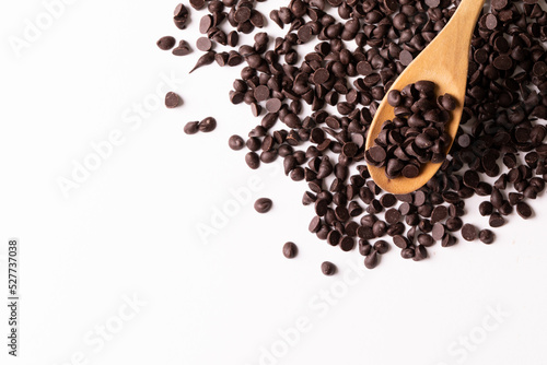 Overhead view of wooden spoon over fresh chocolate chips on white background with copy space