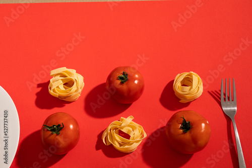 Overhead view of tomatoes and ribbon pasta with fork and plate by copy space over red background
