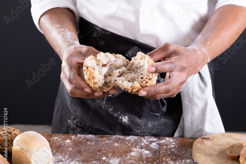 Midsection of african american male baker breaking baked bread over table