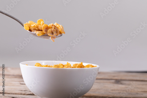 Close-up of cornflakes in spoon over breakfast bowl on table against gray background
