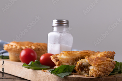 Stuffed pies with tomatoes, herbs and salt shaker on serving board against gray background