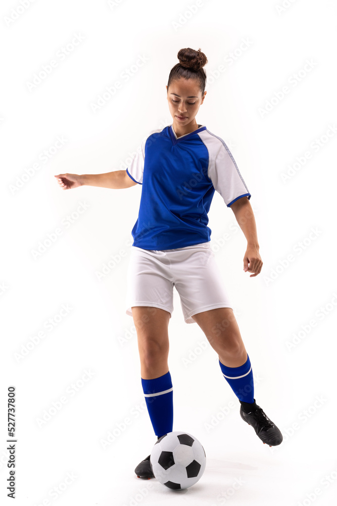 Full length of biracial young female soccer player kicking soccer ball against white background