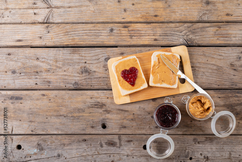 Overhead view of open face peanut butter and jelly sandwich on serving board with jars at table