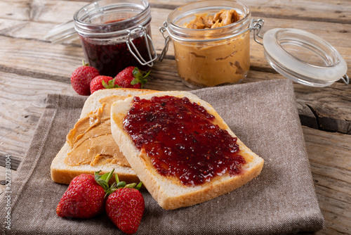 Open face peanut butter and jelly sandwich on napkin with jars and strawberries at table