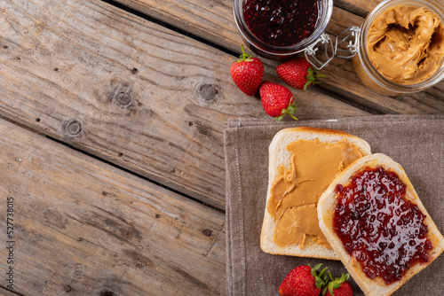 Overhead view of open face peanut butter and jelly sandwich on napkin with jars and strawberries