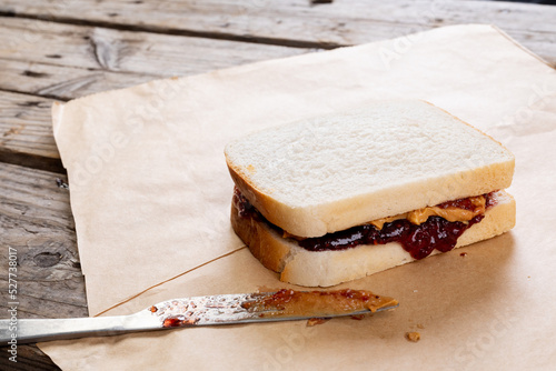 Peanut butter and jelly sandwich on brown paper with table knife at table