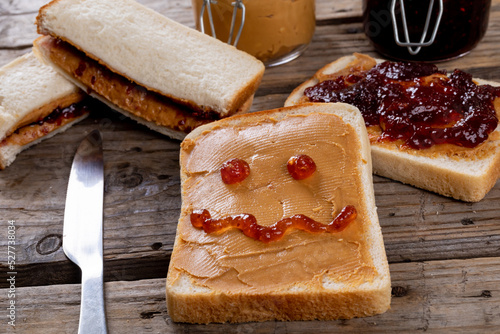 Anthropomorphic face on bread with peanut butter by table knife, sandwiches and jars on table