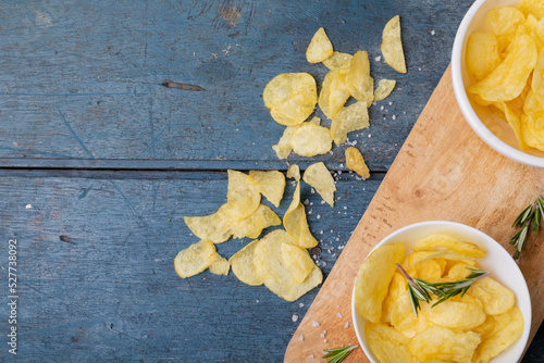 Directly above shot of potato chips in bowl with rosemary on serving board at wooden table