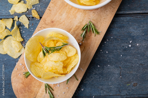 Close-up of potato chips in bowl with rosemary on serving board at wooden table