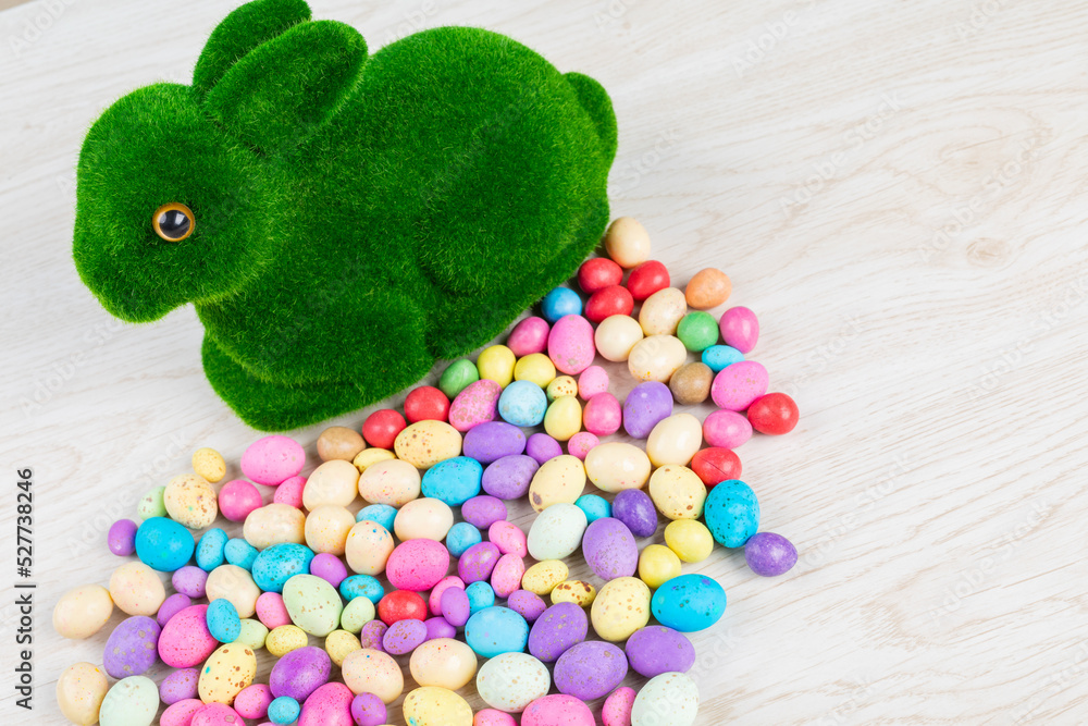 Fototapeta premium High angle view of artificial moss bunny with colorful candy easter eggs on table