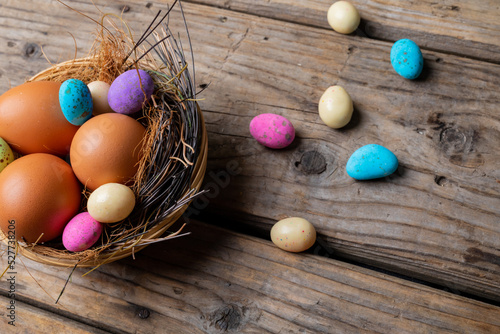 Easter eggs with colorful candies in nest on wooden table