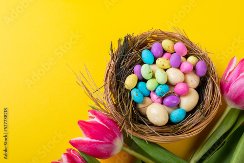 Close-up of colorful easter eggs and candies in nest with tulips on yellow background