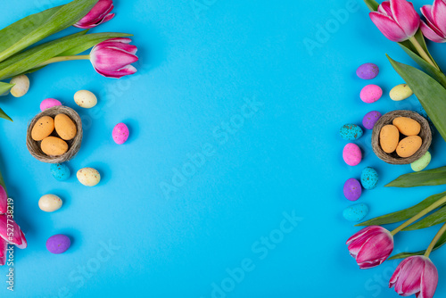 Easter decoration with tulips and colorful candies on blue background with copy space