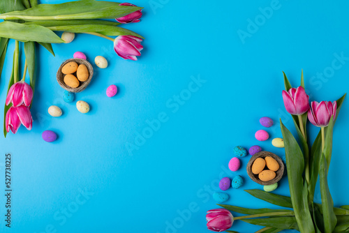 Overhead view of easter candies in small nests with pink tulips on blue background with copy space