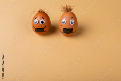 Doodle eyes, eyebrow and mask drawing on easter eggs with strings on top against orange background
