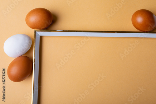 Close-up of brown and white easter eggs around empty frame on orange background