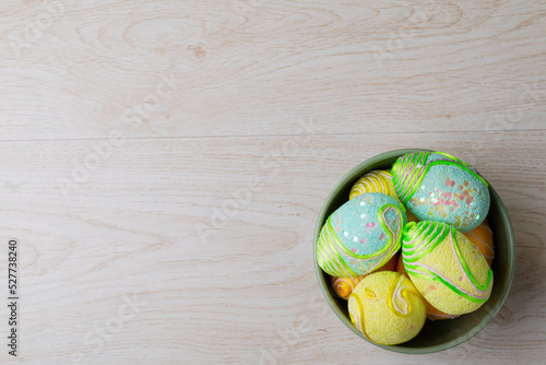 Overhead view of decorated easter eggs in bowl on table with empty space