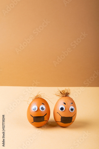 Brown easter eggs with mask painting and doodle eyes against orange background with copy space