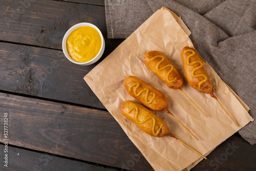 High angle view of mustered sauce on corn dogs over paper bag at wooden table