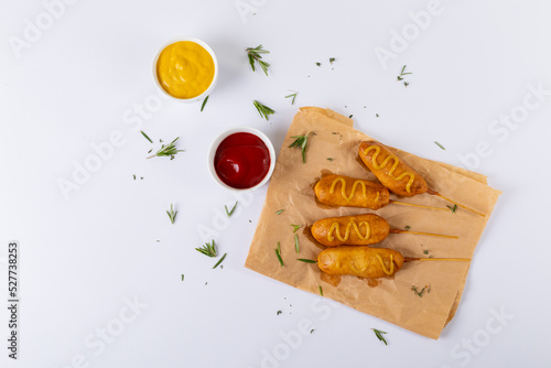 Corn dogs with rosemary on paper bag by mustered and tomato sauces over white background