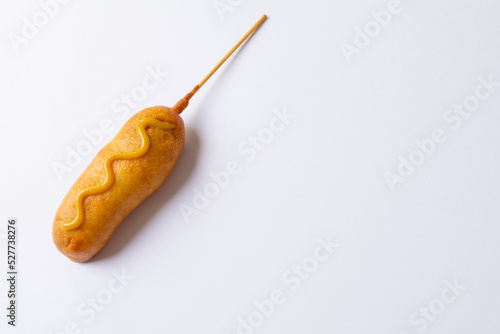 Close-up of corn dog with mustered sauce over skewer on white background with copy space