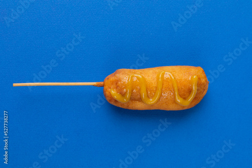 Close-up of corn dog with mustered sauce over skewer on blue background with copy space