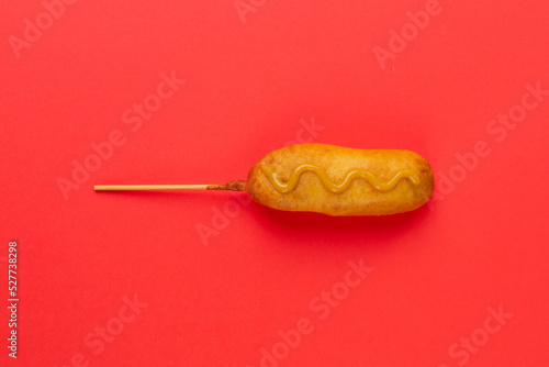 Overhead view of corn dog with mustered sauce over skewer on red background with copy space