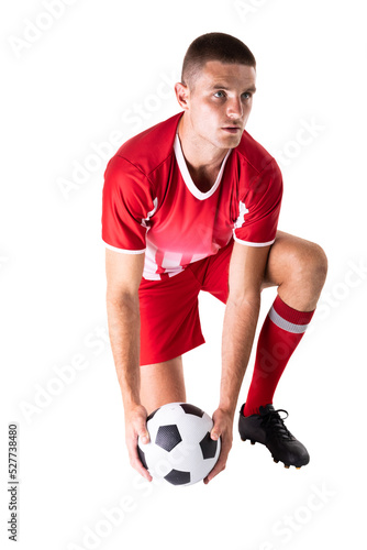 Confident young male caucasian soccer player kneeling while holding ball against white background