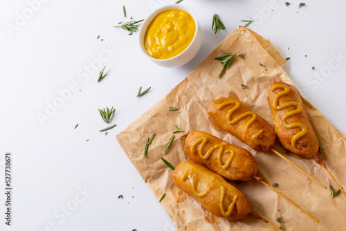 Corn dogs with mustered sauce and rosemary on paper bag on white background