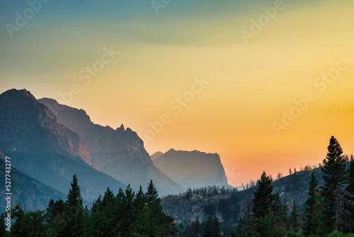 Mountain peaks in the mountains of Glacier National Park in Montana at sunrise or sunset with the haze from the wildfire smoke filling the sky and valley looking like mist or fog