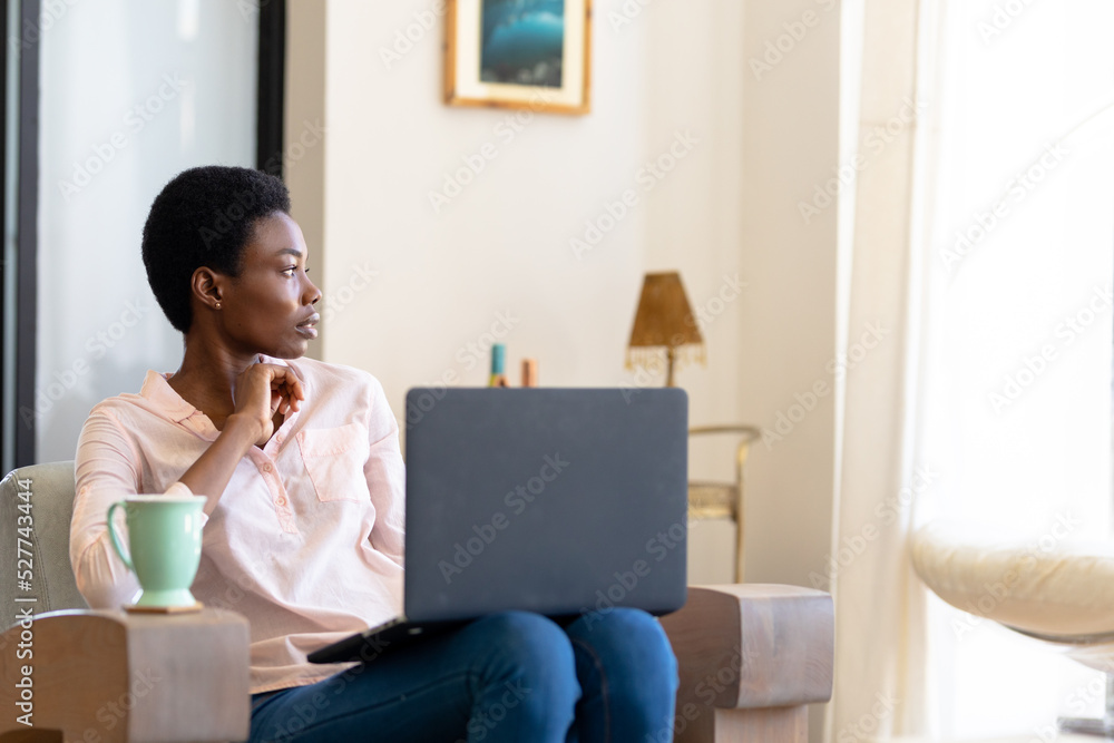 Thoughtful african american woman sitting on sofa with laptop and coffee cup in living room at home Thoughtful african american woman sitting on sofa with laptop and coffee cup in living room at home