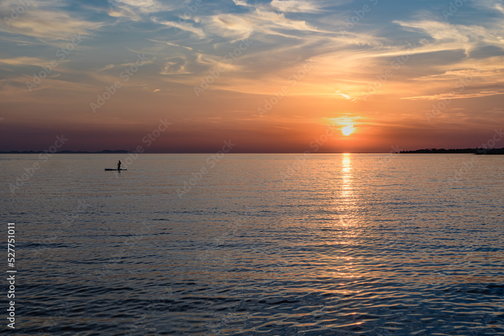 Silhuette of girl on sup board with beautiful colored sunrise background, Zaton, Croatia