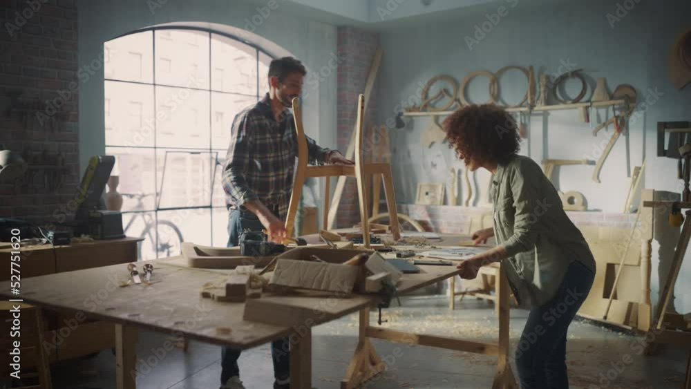 Small Business Owners of a Furniture Store Working on a New Wooden Dining Table Chair. Carpenter Building the Chair, While Young Female Manager Using Laptop Computer. Small Business Owners of a Furniture Store Working on a New Wooden Dining Table Chair. Carpenter Building the Chair, While Young Female Manager Using Laptop Computer.