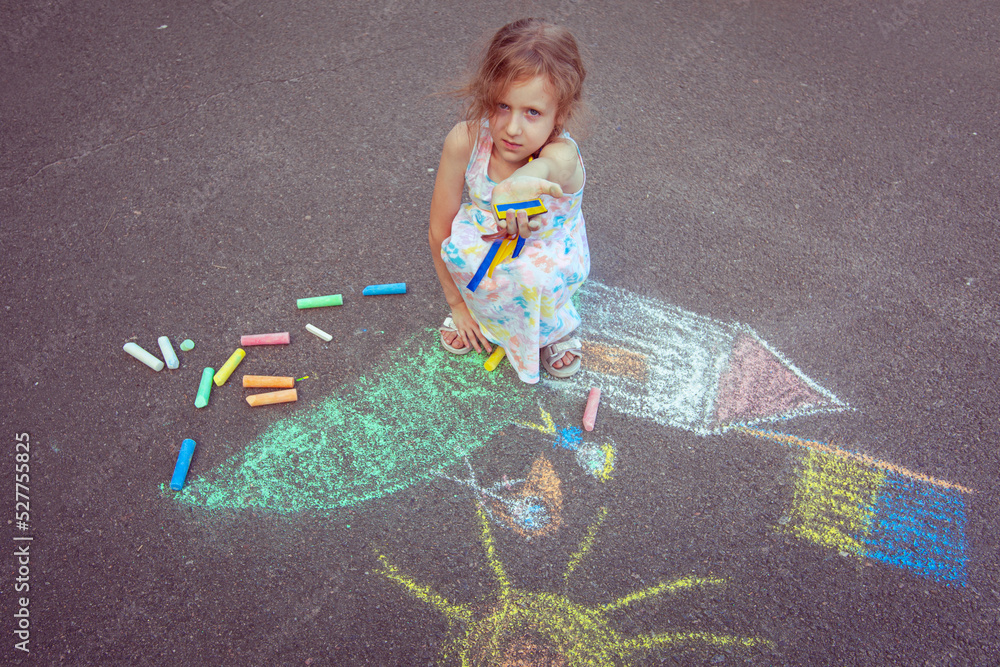 Fototapeta premium Ukrainian girl child draws children's drawings with chalk on the pavement.