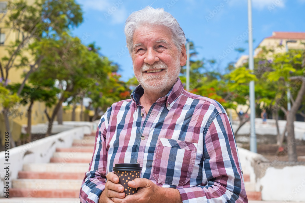 Smiling elderly man in summer holiday walking in the city with a takeaway coffee cup in hand Smiling elderly man in summer holiday walking in the city with a takeaway coffee cup in hand