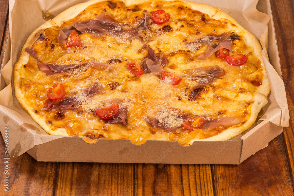 Pizza with ham in pizza cardboard box on rustic table