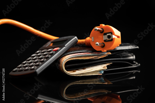 Fotografija Orange electric plug, wallet with money and calculator on black background