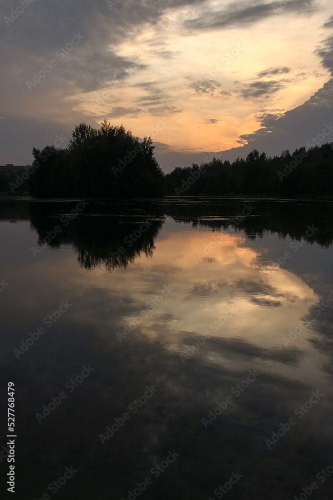 Dramatic sky with sun shines through gray clouds reflected at lake water at night