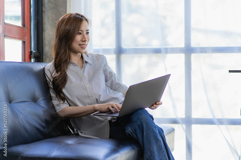 Asian woman working with laptop on sofa at home watching movies listening to music surfing the internet Asian woman working with laptop on sofa at home watching movies listening to music surfing the internet