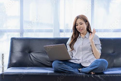 Asian woman working with laptop on sofa at home watching movies listening to music surfing the internet