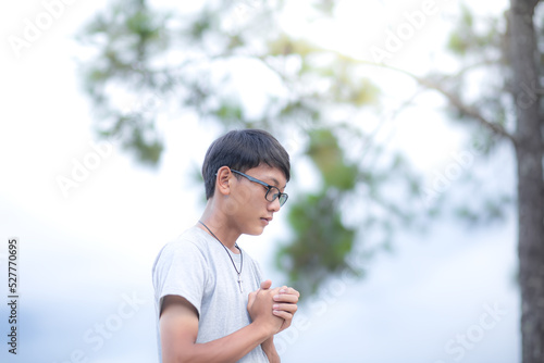 Handsome boy christian in glasses. young man praying to God near a tree. concept religion. focus on face. Copy space for your individual text.