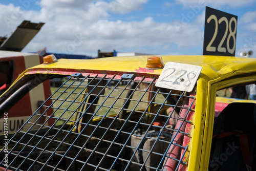 Closeup of a dented yellow stock car with number 228 and wire mess instead of a windshield on a sunny day with clouds. photo